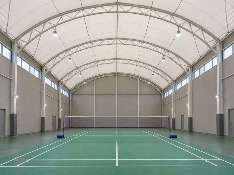 Enclosed single badminton court hall beneath a white tensile membrane roof