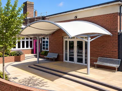 White curved fabric entrance canopy on grey steel posts outside a brick building