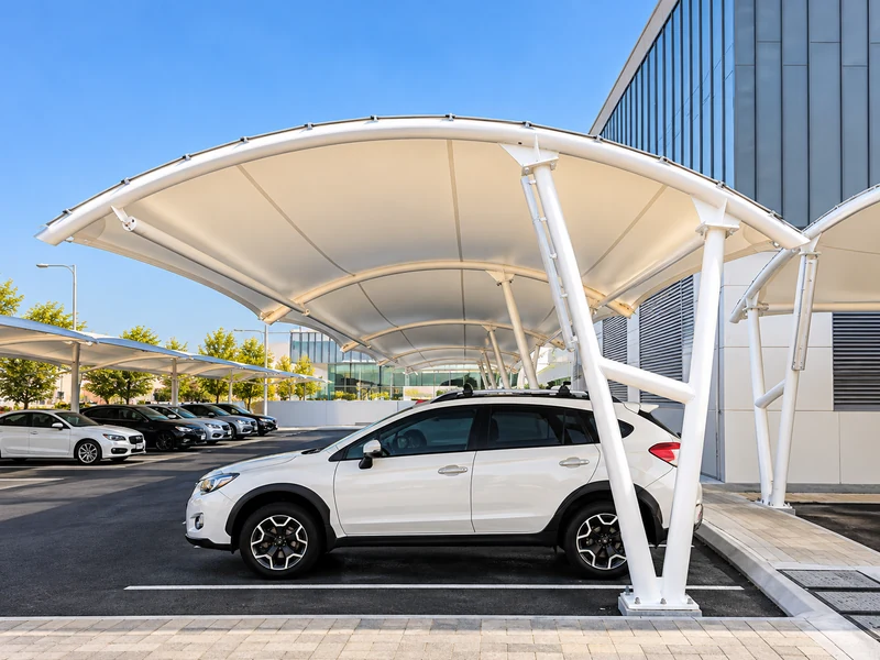 White curved carport canopy sheltering parked cars beside a modern building