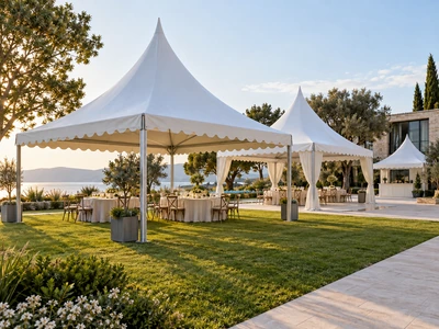 White high-peaked pagoda tents with dining tables on a landscaped lawn beside the water
