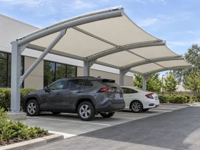 Cantilever car parking shed with rear steel columns, diagonal braces and bolted base plates supporting a white fabric roof