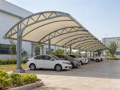 Fabric parking shed with steel roof trusses covering vehicles outside a factory