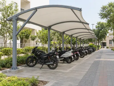 Curved fabric shed on braced steel supports over a row of motorcycles and scooters