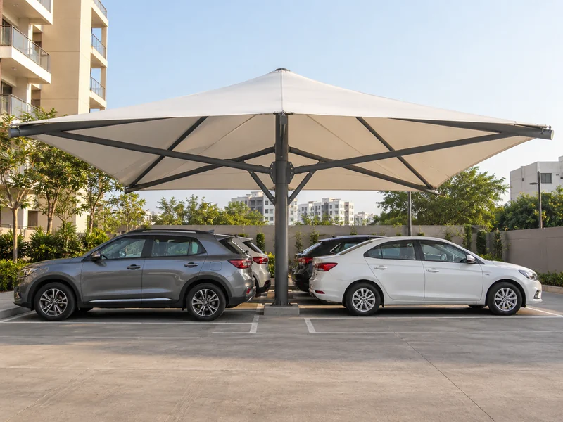 Large square fabric umbrella on a single central mast shading four parked cars around it