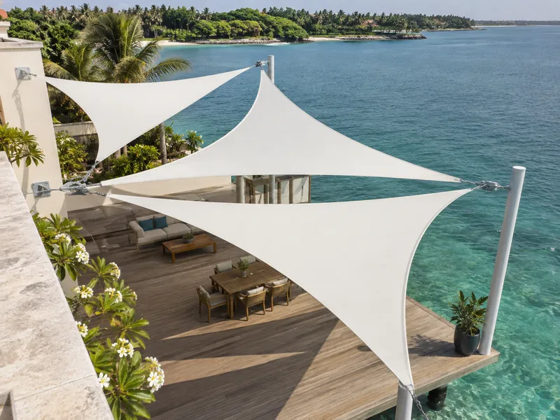 Aerial view of white triangular shade sails arranged above a wooden deck over turquoise water