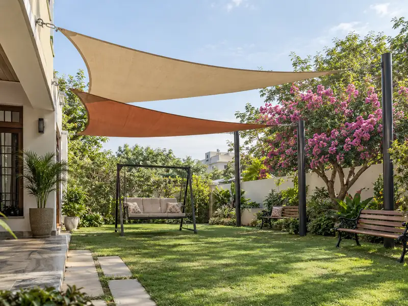 Two sails at different heights over a lawn swing and benches beside a flowering tree