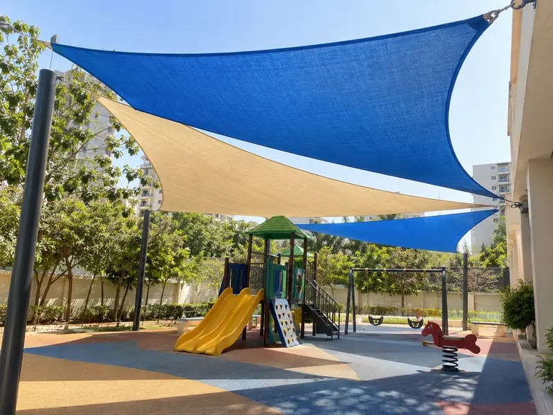 Bright blue and sand HDPE shade sails over a playground with dappled shade on the ground
