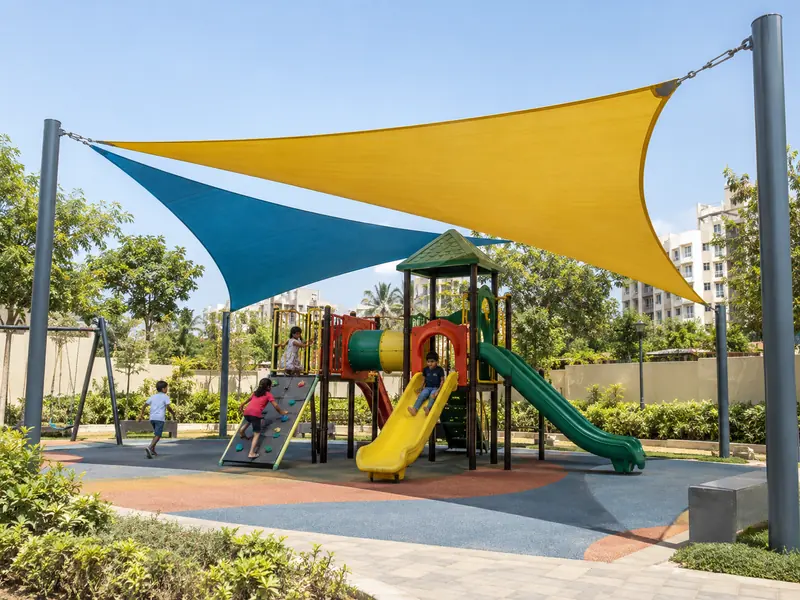 Children playing on a jungle gym under a bright triangular shade sail with posts outside the play area