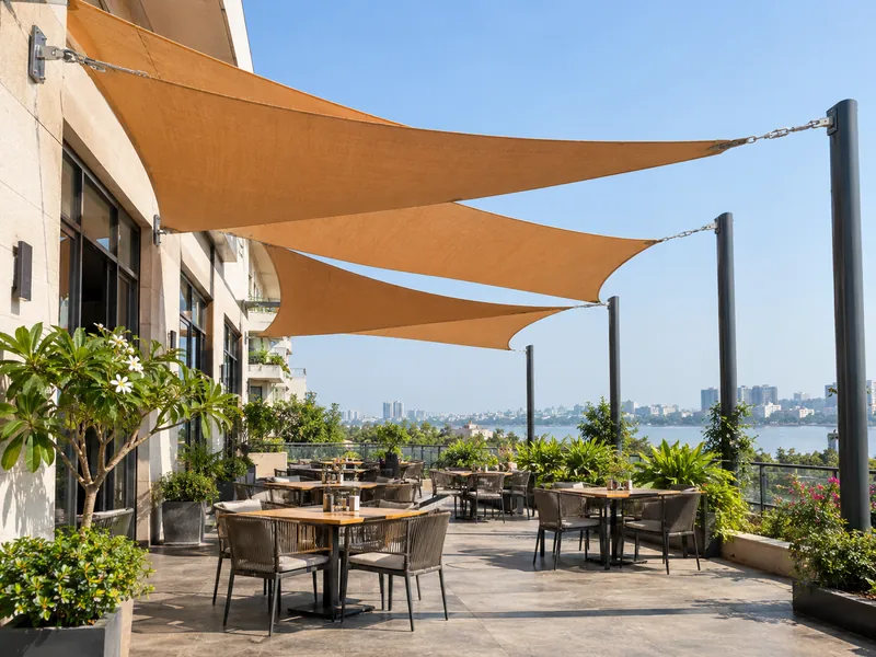Café terrace with brand-coloured shade sails fixed to the building wall and posts over dining tables