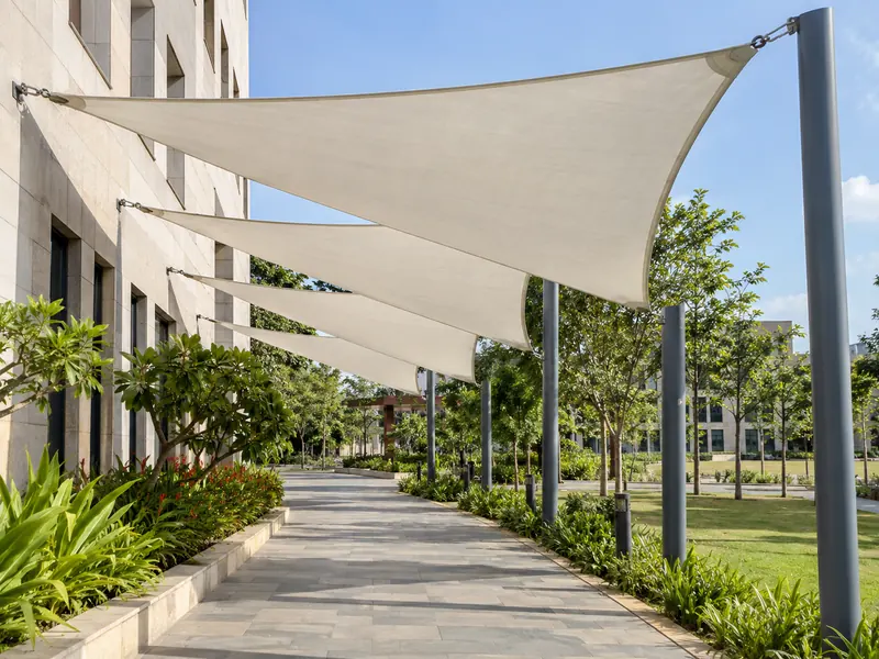 Row of staggered white shade sails over a campus footpath with posts along one side