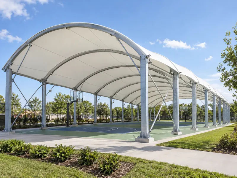 Long white fabric roof on repeated curved steel arches over an outdoor sports court