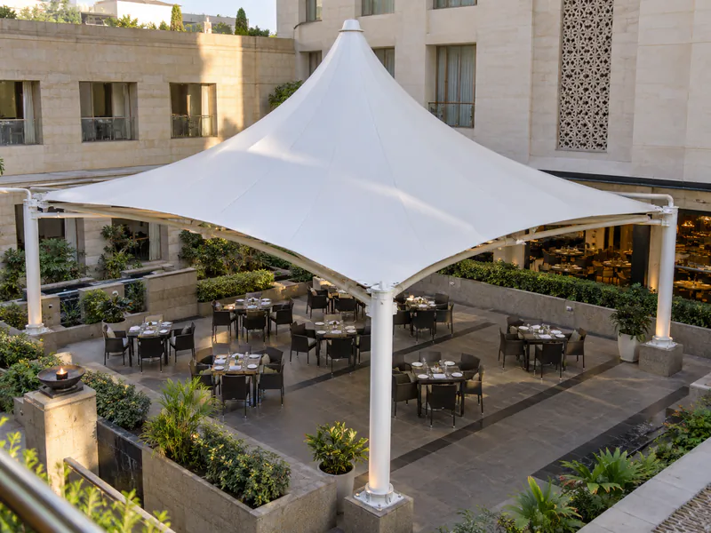 White peaked tensile canopy on perimeter columns above courtyard dining tables