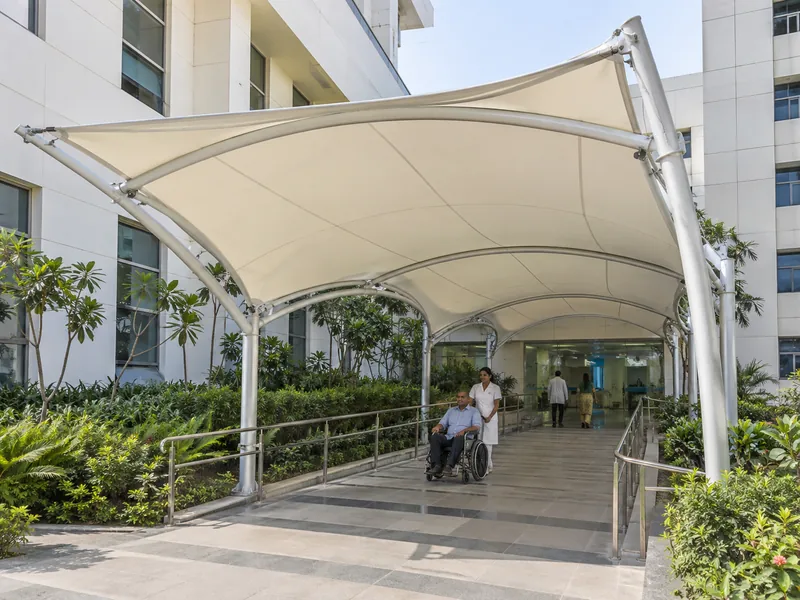 Fabric-roofed corridor linking two hospital buildings, with a wheelchair user passing underneath