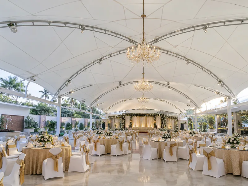 Inside a column-free banquet hall under a white tensile roof with chandeliers hung from the steel frame