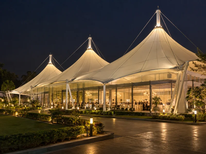 Multi-peak fabric roof over an event hall with glass side walls lit up at night