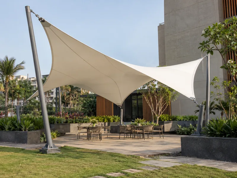White saddle-shaped fabric canopy with two high and two low corners on steel masts over garden seating