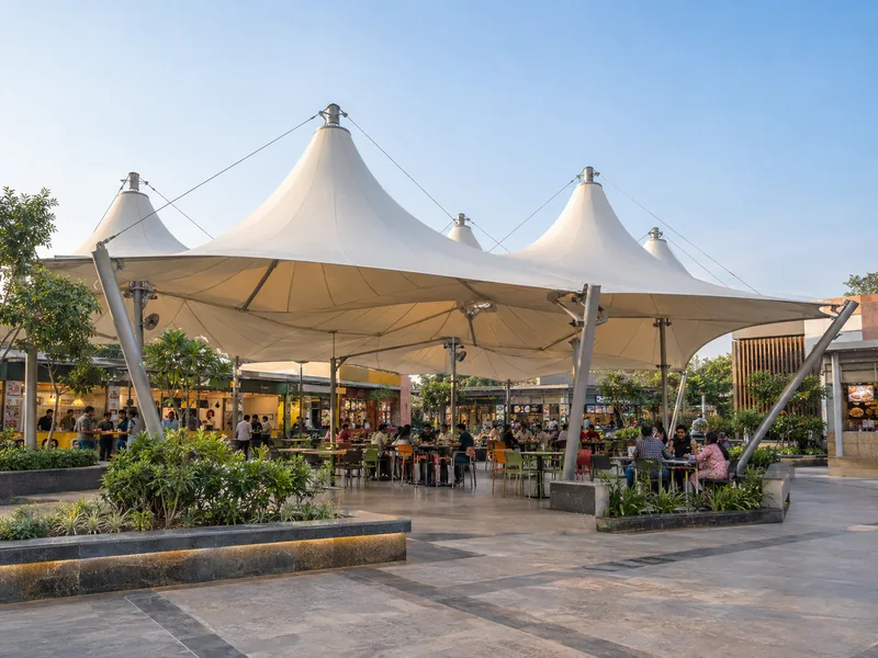 Large multi-cone fabric roof over shared seating in an open-air food court with stalls around it