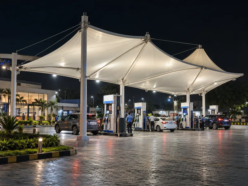 Petrol pump forecourt at night with lights under a tensile canopy and cars at the pump islands
