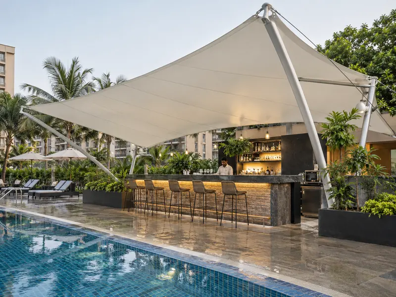 Membrane canopy over a poolside bar counter with stools on a wet tiled deck