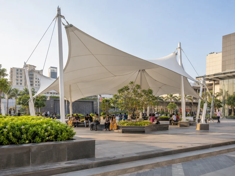 Tall mast-supported white fabric canopy over a busy city plaza with people seated on benches below