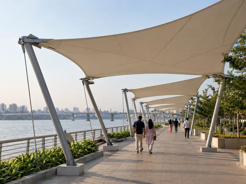 Line of membrane shades along a riverfront promenade with walkers passing in the shade