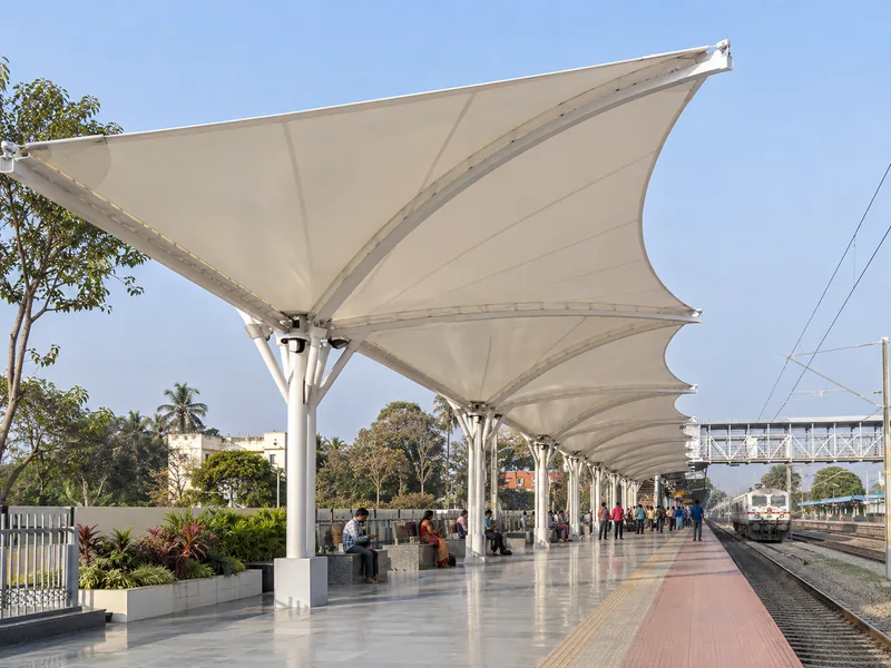 Long butterfly-shaped fabric roof on a single row of columns along a railway station platform