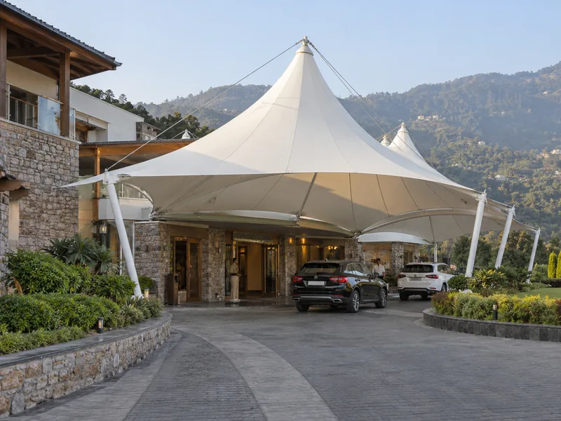 Peaked white fabric canopy over the arrival porch of a hill resort with cars at the entrance