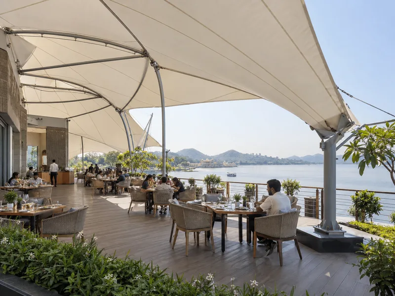 Tensile roof over a resort restaurant deck facing a lake, with diners seated beneath