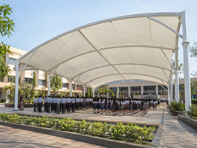 Students standing in rows under a large white arched fabric canopy over a school assembly ground