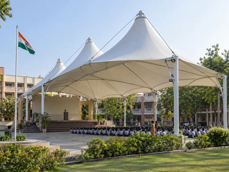 Multi-cone tensile roof over a school assembly area with a podium at one end and the flagpole outside