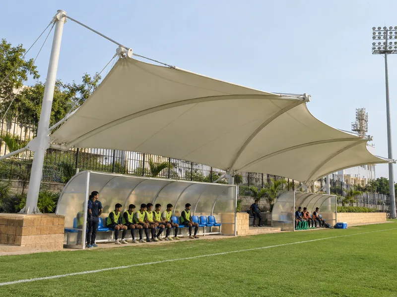 Tensile canopy over players' dugout benches at the edge of a football field