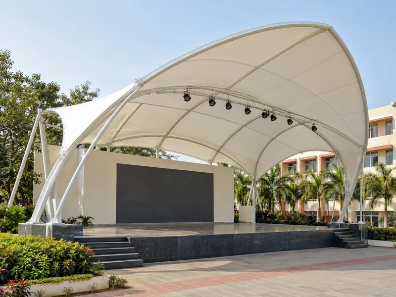 Shell-shaped white fabric roof over an open-air school stage with lights hung from the steel frame