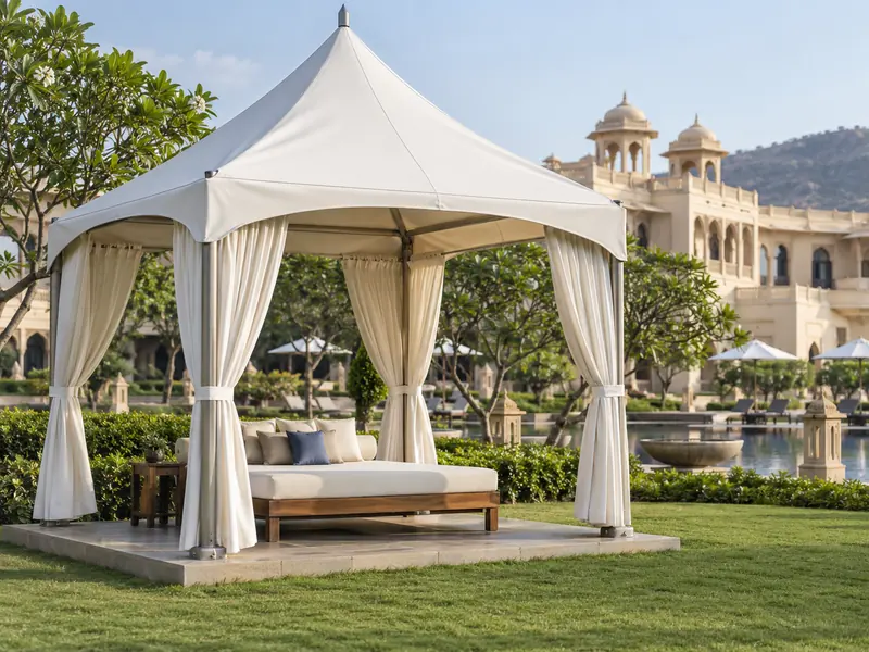 White peaked fabric cabana with tied-back side curtains over a day bed on a resort lawn