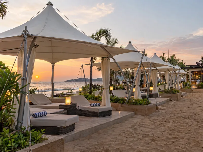 Row of tensile cabanas along a beach club with loungers and soft lights inside