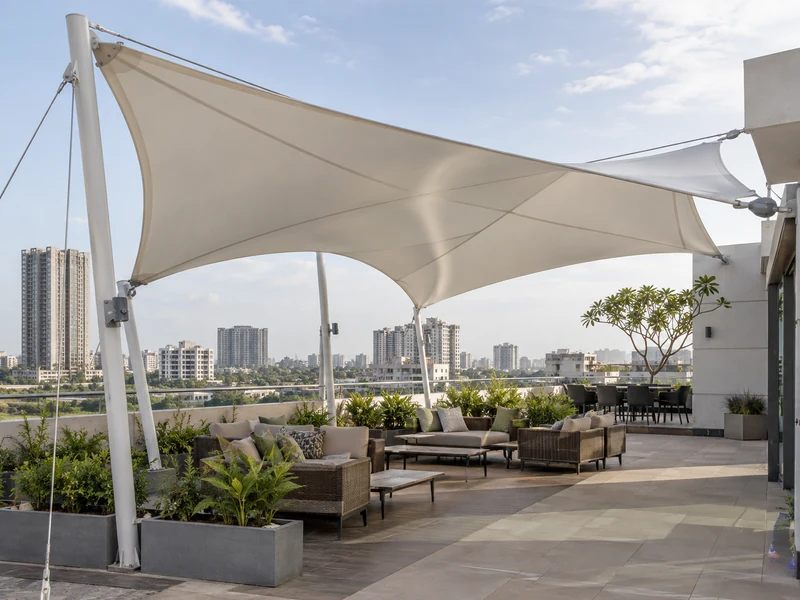 White fabric canopy over a rooftop terrace seating area with city buildings in the background