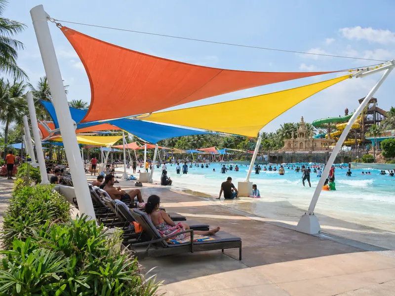 Colourful fabric shade sails over the loungers beside a wave pool in a busy water park