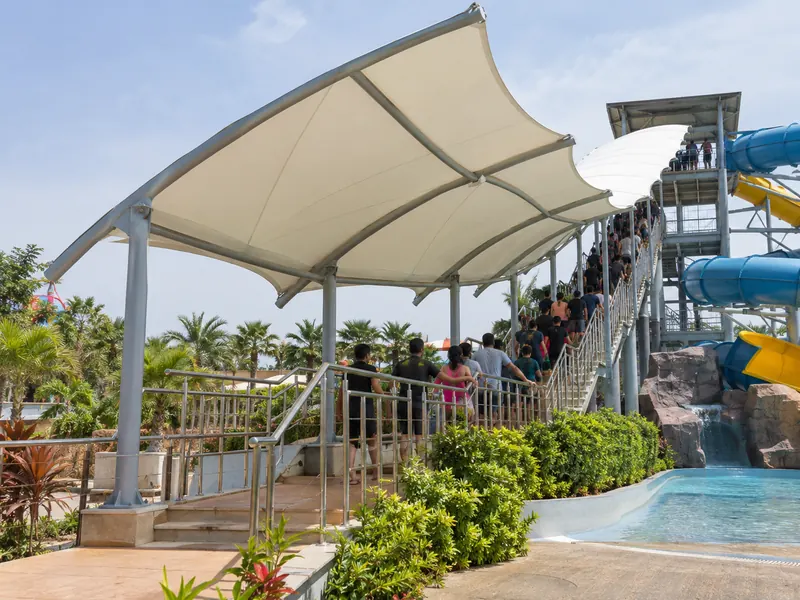 Long tensile canopy over a water slide queue line with stairs going up to the slide tower