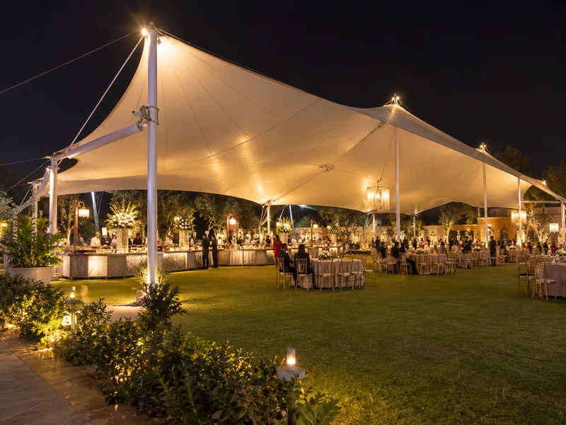 Large tensile roof over buffet counters and dining tables on a lit wedding lawn at night