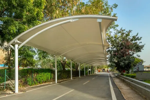 A white fabric canopy covers a park road, creating a shaded walkway structure for visitors to enjoy a
                                                    pleasant stroll.